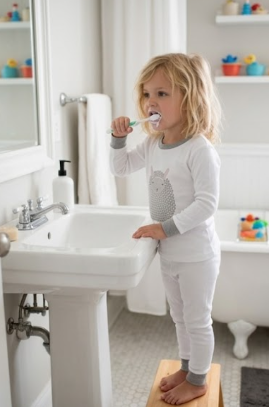 Child in the Nene Kids Lamb pajama set brushing their teeth at the bathroom sink