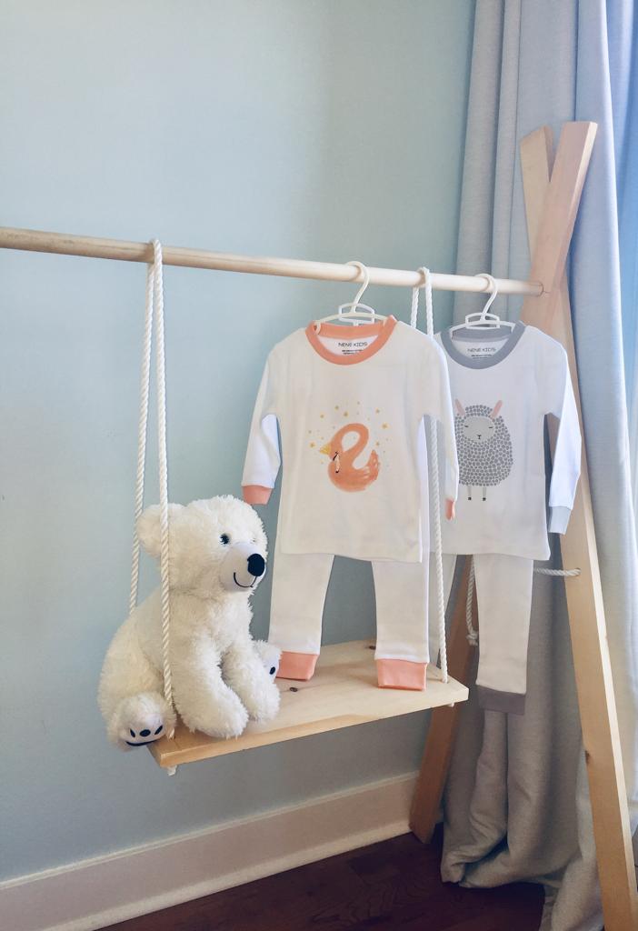 Nene Kids Lamb and Pink Swan pajama sets hanging on a wooden rack in a nursery