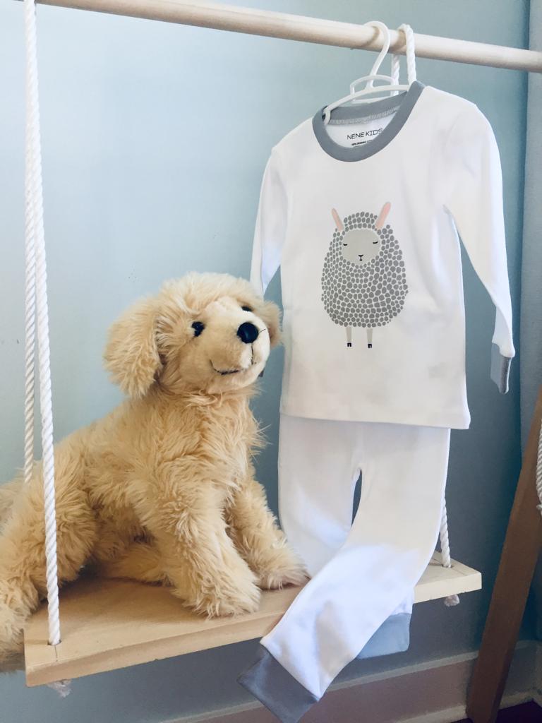 Lamb pajama set hanging on a wooden rack beside a plush puppy